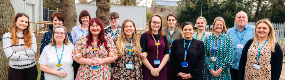 A group of staff wearing ID badges stand outside smiling
