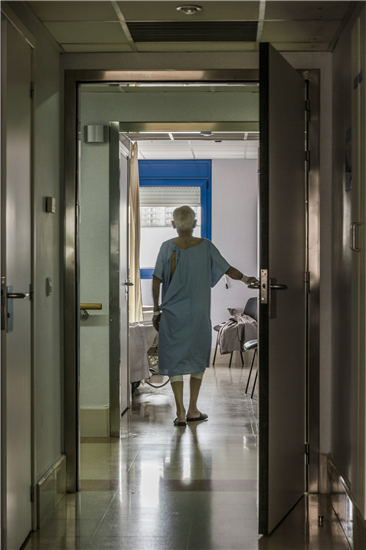 Older person stands almost in sillouette in a hospital corridor