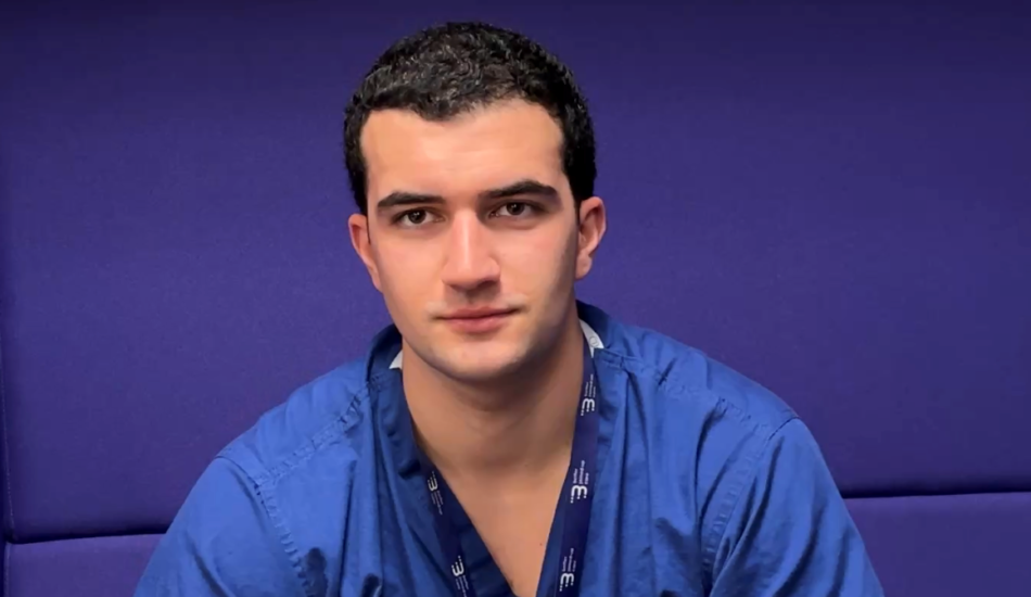 Resident Dr wearing blue scrubs in front of a purple background